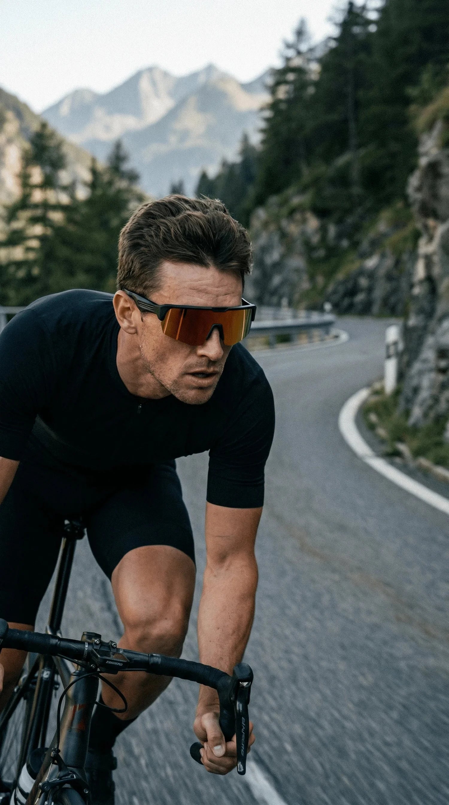 Homme en plein effort sur vélo de route portant des lunettes connectées Noctavy avec verres miroir orange, sur une route de montagne.